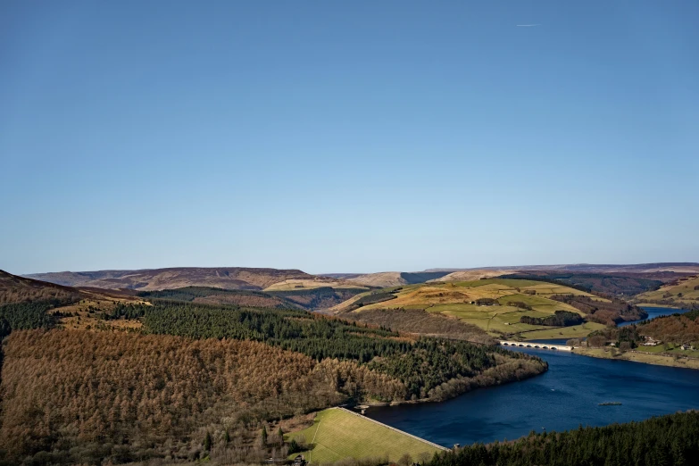 a hill overlooking a river, mountains and fields