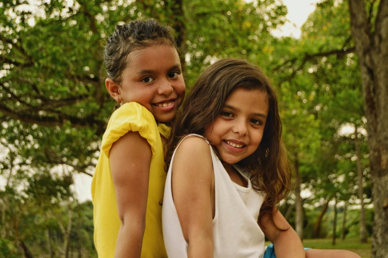 two little girls one wearing a white top is holding on to the other with her arms