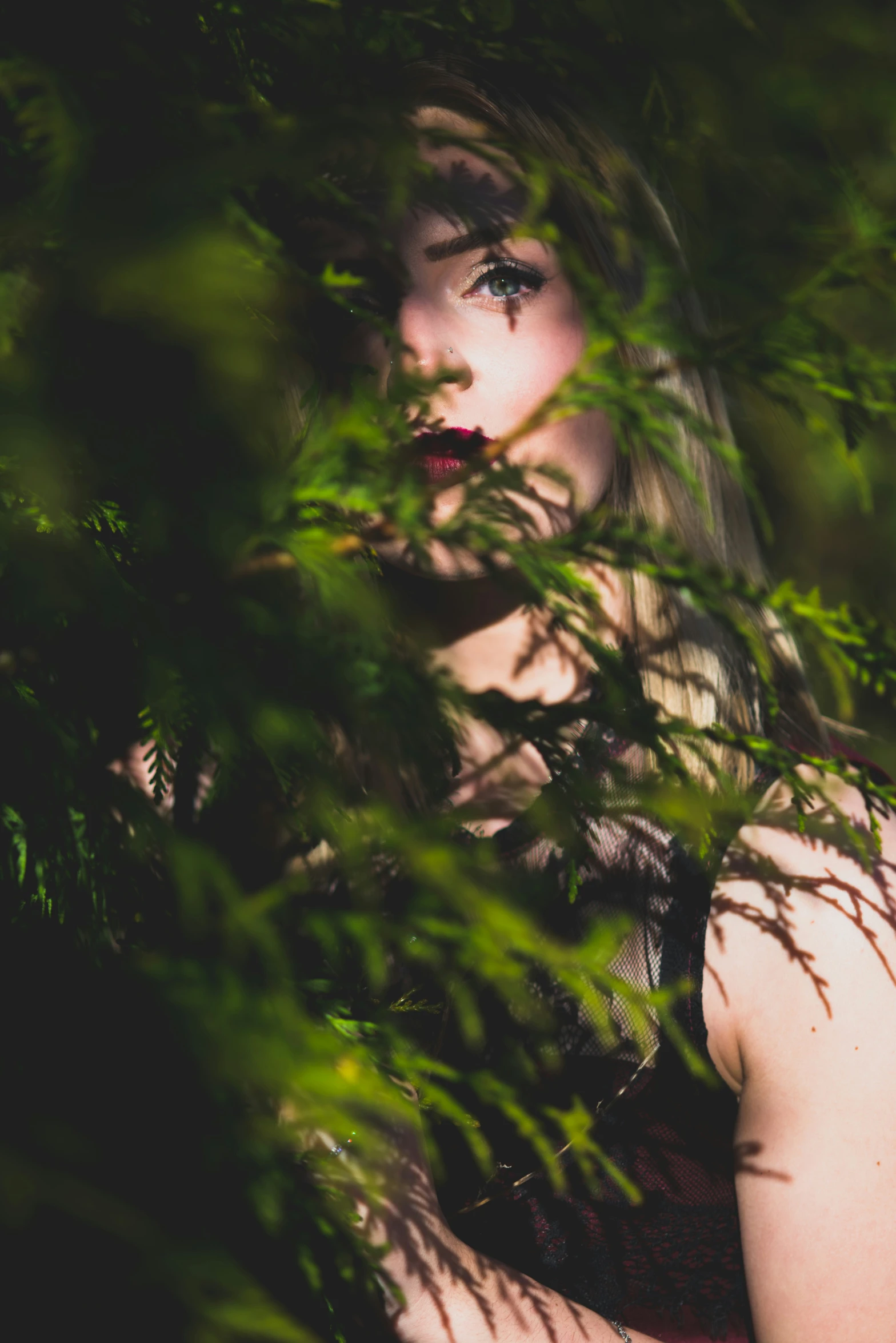 the young woman with blonde hair is hiding behind some green leaves