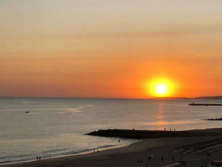 the sun sets over the ocean at a sandy beach