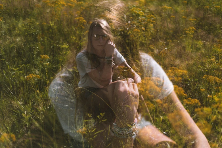 a girl sitting in tall grass holds an object up to her face