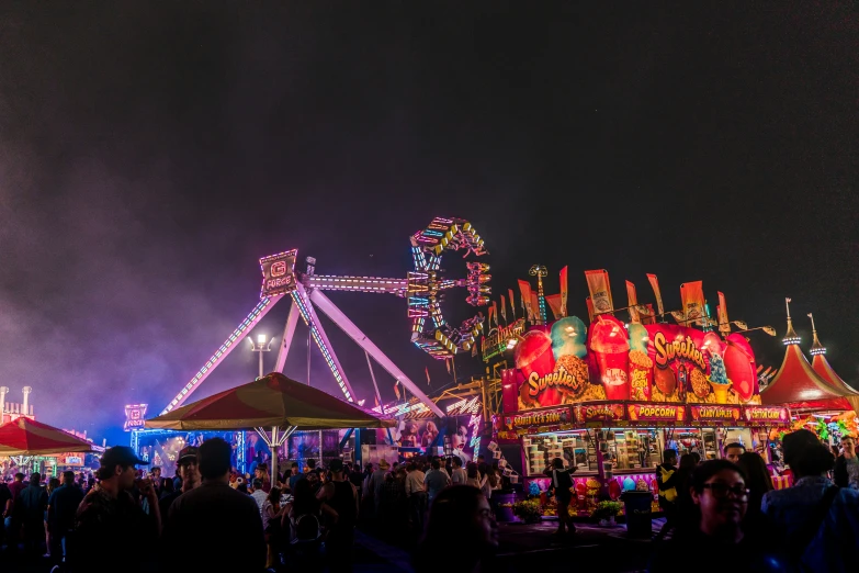 an elaborate ferris wheel and several decorated booths at night