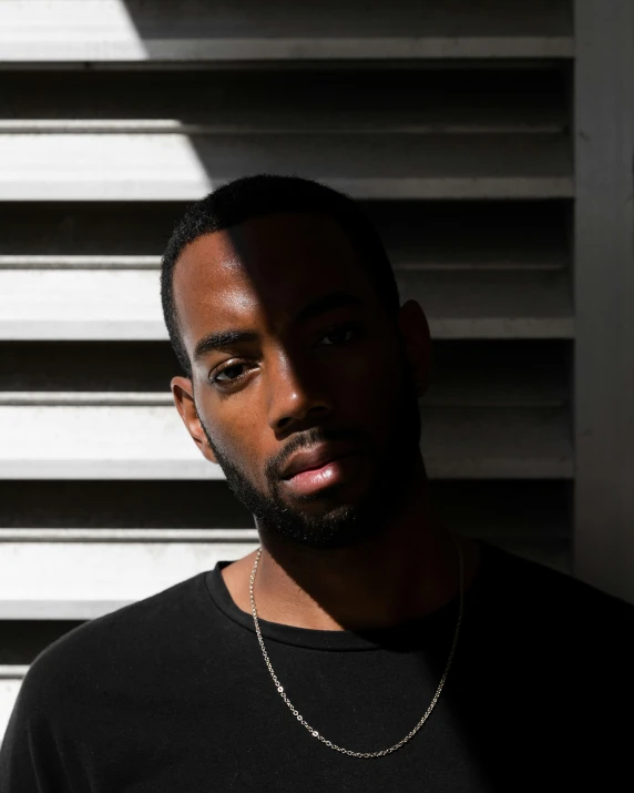 black male in black shirt against white wall