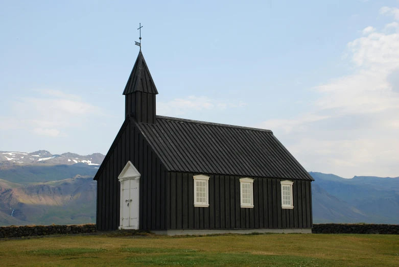 a black church with an open front door and a steeple is surrounded by mountains