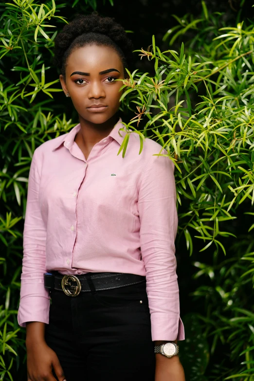 a woman stands in front of bushes with a pink shirt