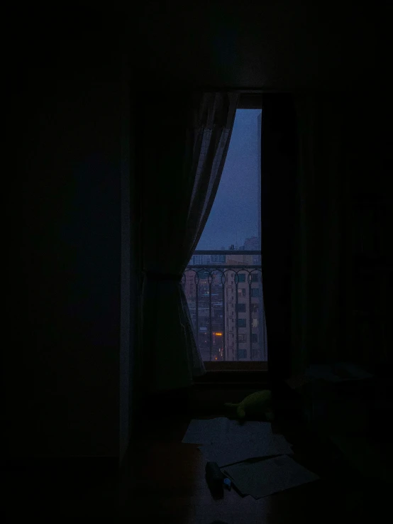 an open window with curtains and buildings outside at night