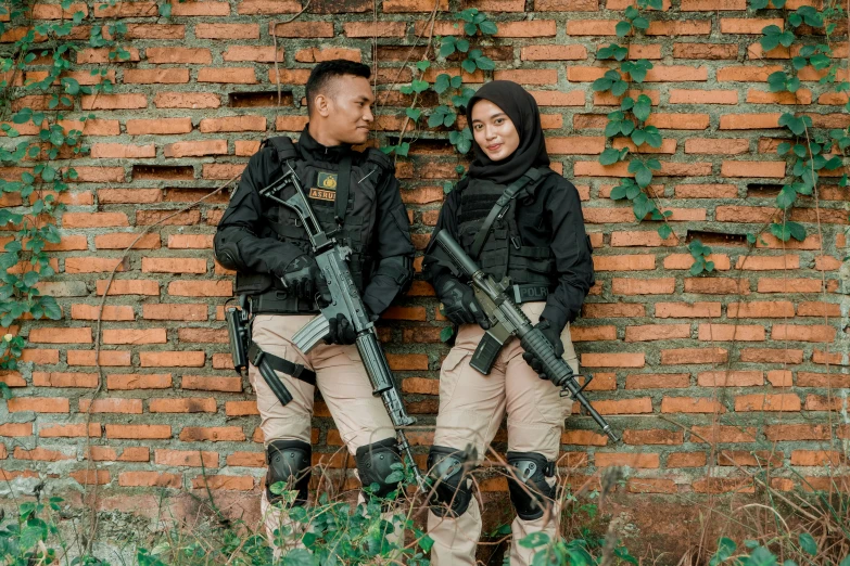 two military officers holding guns and posing against a brick wall