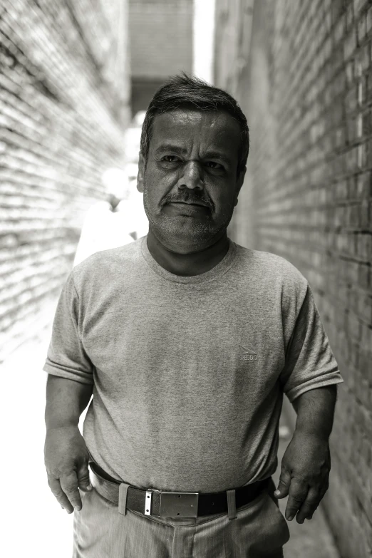 a man in grey shirt standing next to brick wall