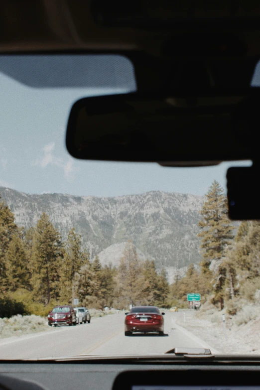 cars moving along a tree covered road in the middle of a mountain range