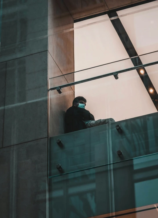 a person wearing a face mask sits on a building ledge