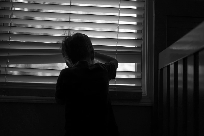 a person who is looking out of a window with blinds on the side