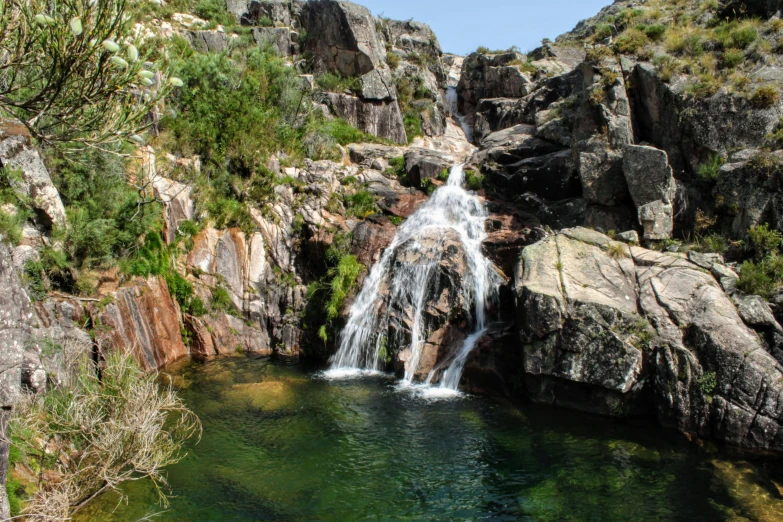 a waterfall coming down into a river surrounded by mountains