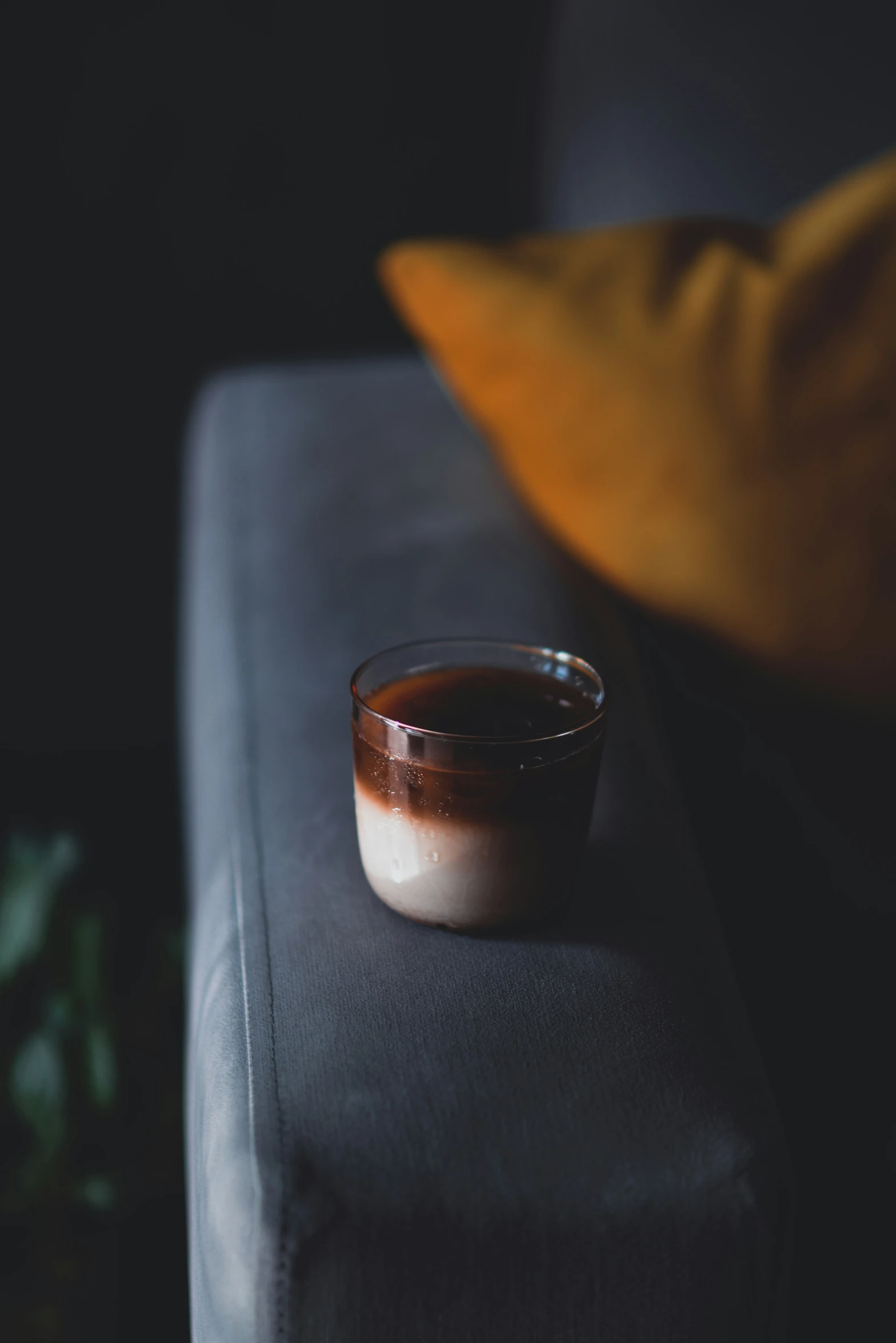 glass cup sitting on a grey couch with black background