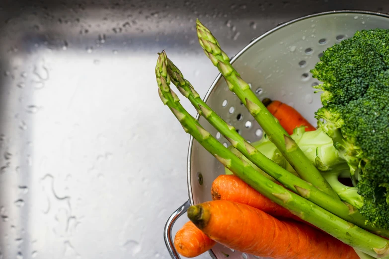 two bunches of broccoli and three carrots in a strainer