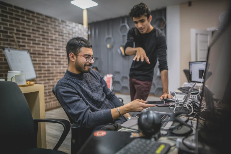 two men sitting at a desk working on a laptop