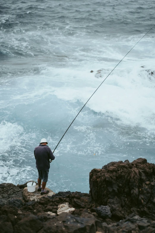 a man standing on a cliff fishing next to the ocean