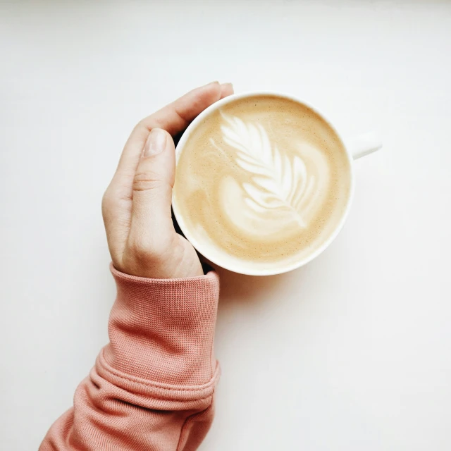 a person holds up a latte with an untrehomable leaf pattern