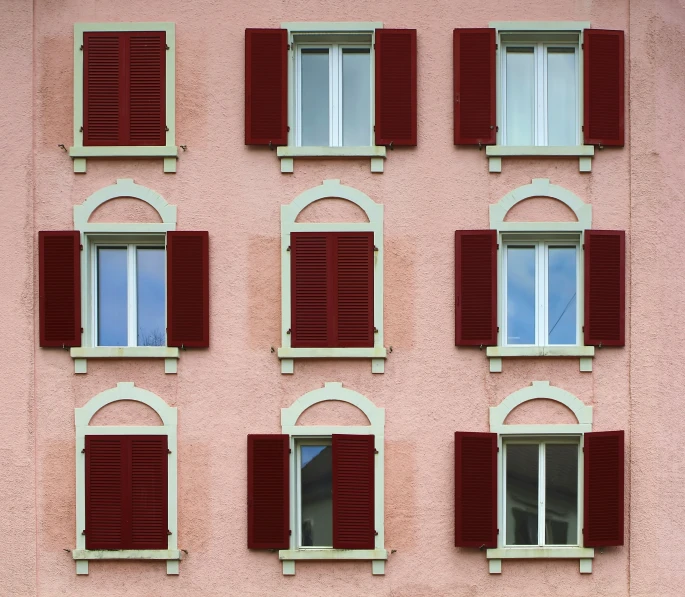 many red windows and some white shutters against a pink wall