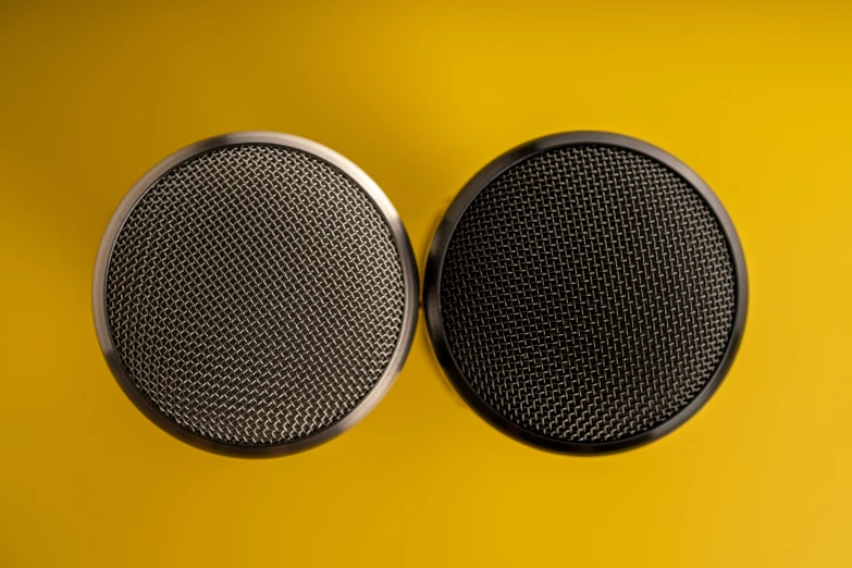 two round speakers side by side sitting on a yellow surface