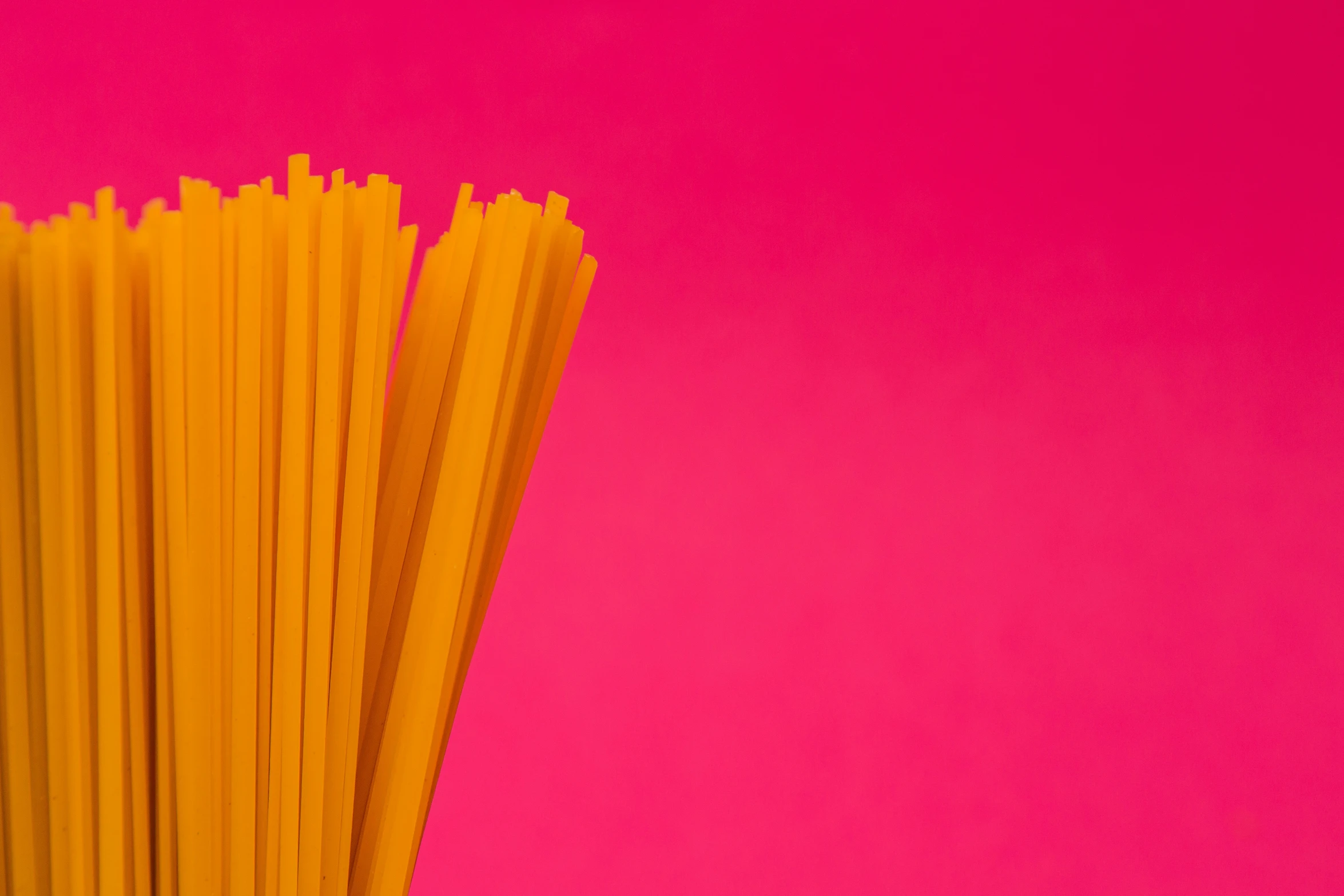 multiple pieces of thin yellow pasta against a pink background