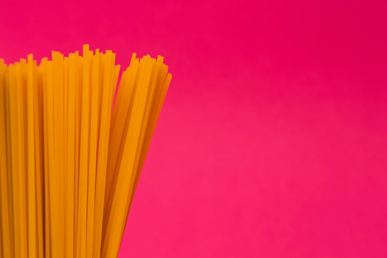 multiple pieces of thin yellow pasta against a pink background