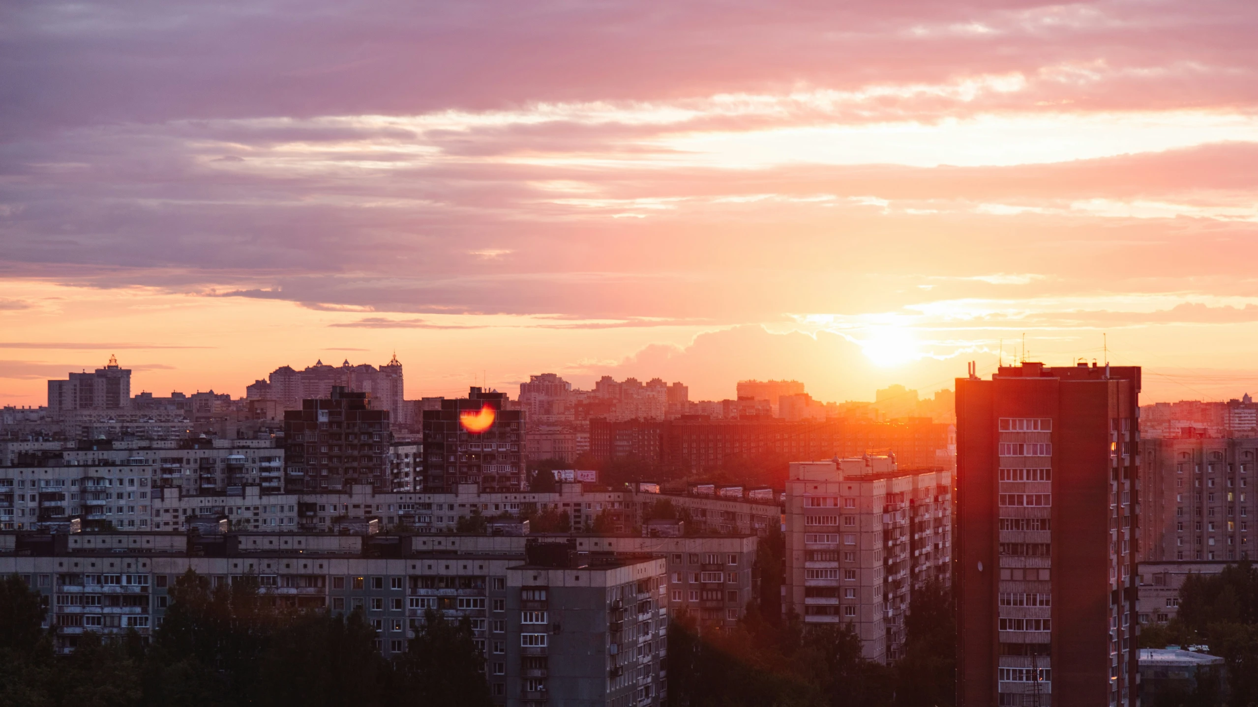 a sunset from a distance, with high rise buildings at the far side