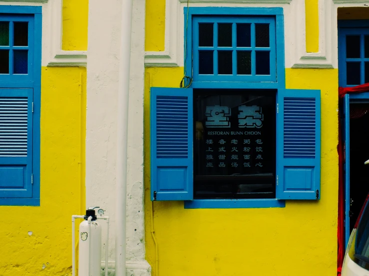 a car is parked in front of a yellow building with blue windows