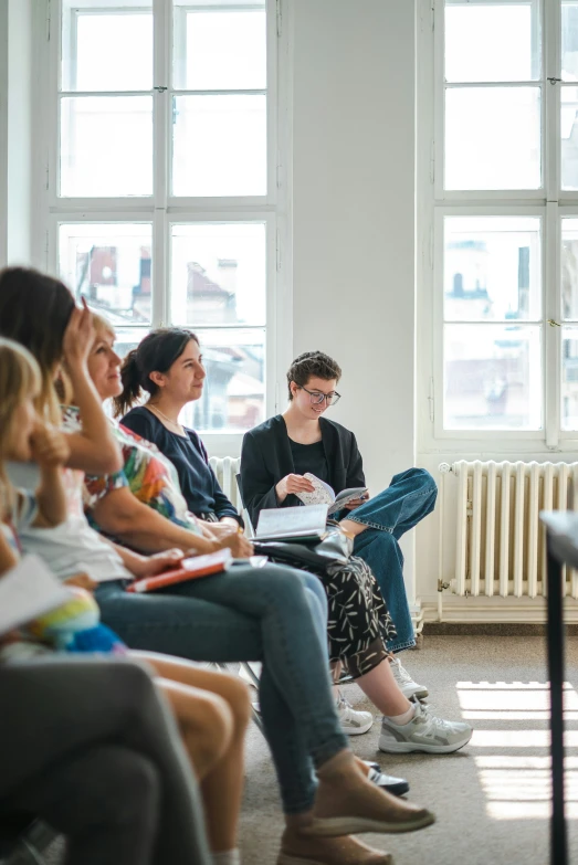 three women sitting in chairs with books and one is reading