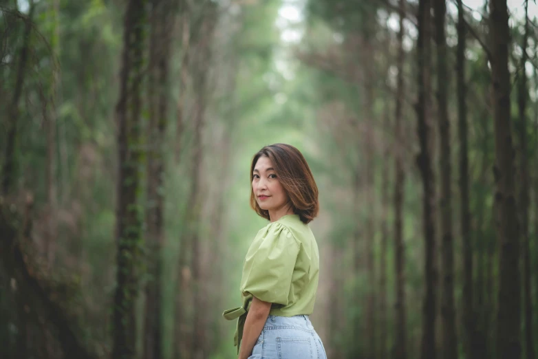 a woman in green shirt and blue jean shorts standing by a tree