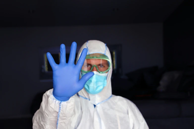 a person in a protective coat and mask and hand wearing protective blue gloves