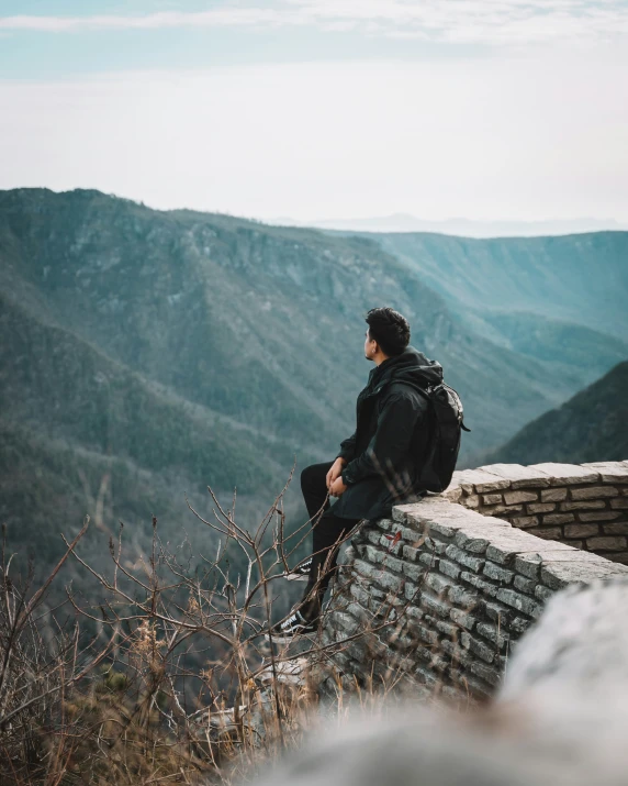 a man is sitting on top of a wall looking out over the mountains