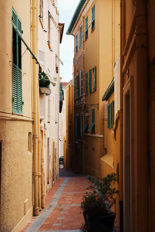 a narrow street with yellow buildings with green shutters
