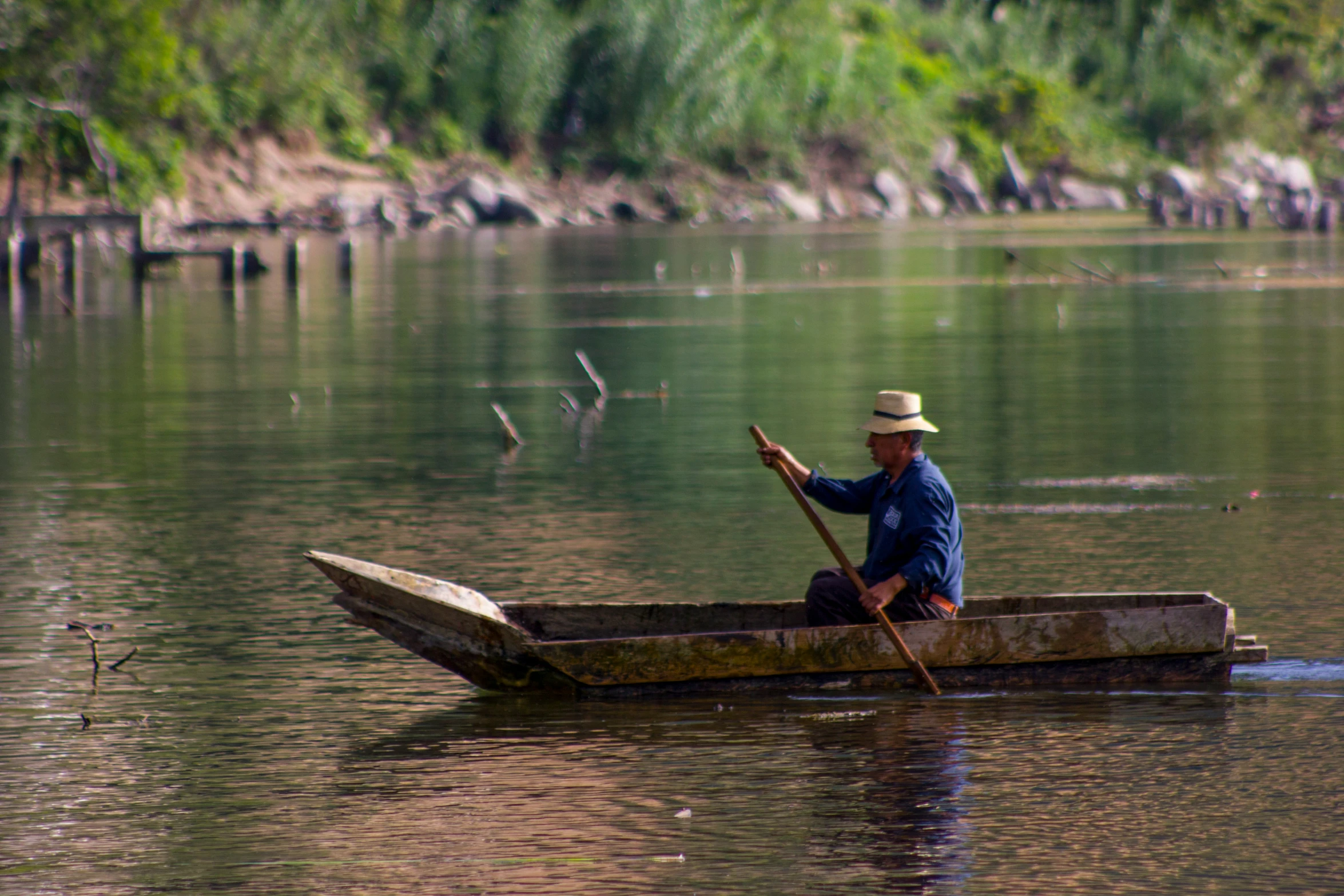 a man in a straw hat paddling a small wooden boat