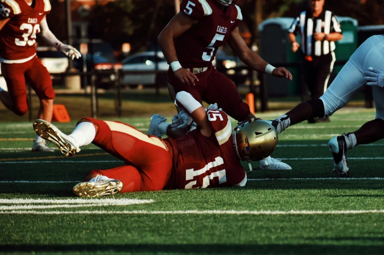 two football players with helmets and pads on the ground, one falling off his feet