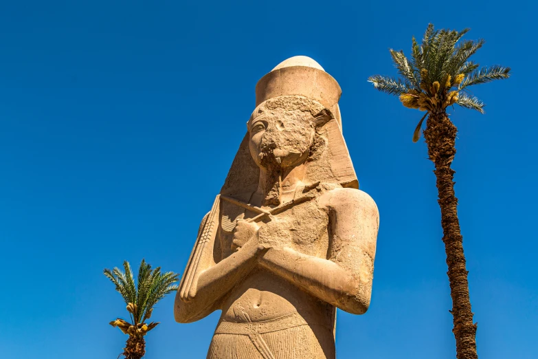 a statue of a sphinx stands near two palm trees