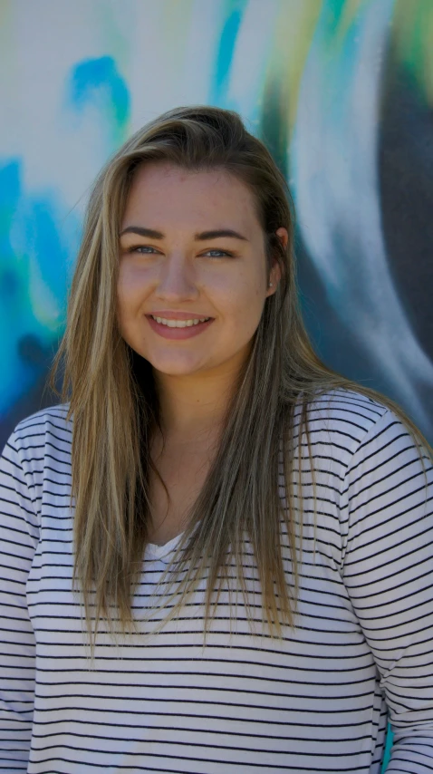 the woman smiles brightly at the camera in front of graffiti