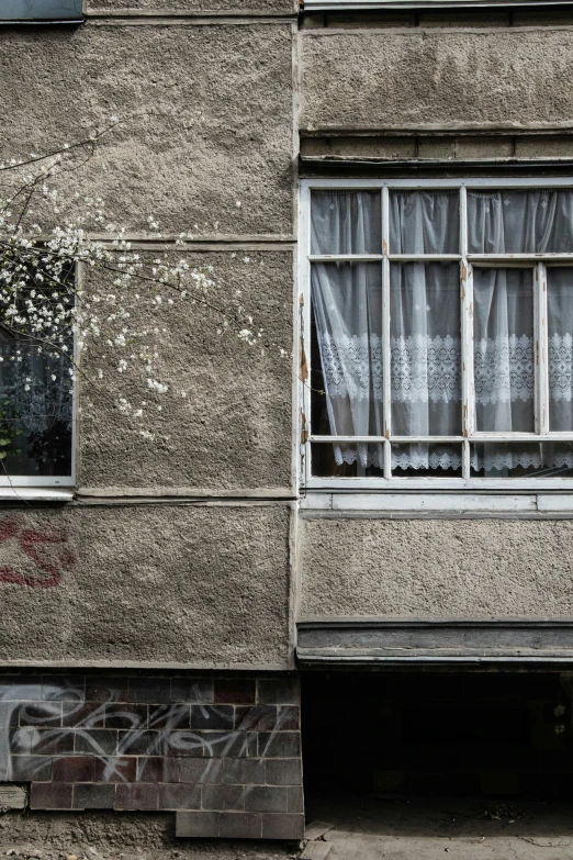 a concrete building with two windows with curtains