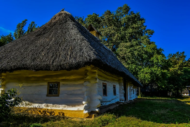 a white thatched cottage on green grass with trees in the background