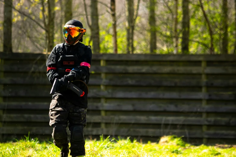 a man in black jacket and yellow goggles standing in grassy area next to forest