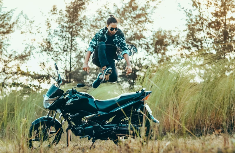 a man jumping off the back of a black motorcycle in a field