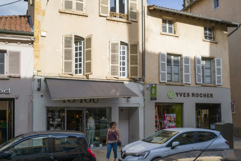 a person standing outside a shop with cars parked in front