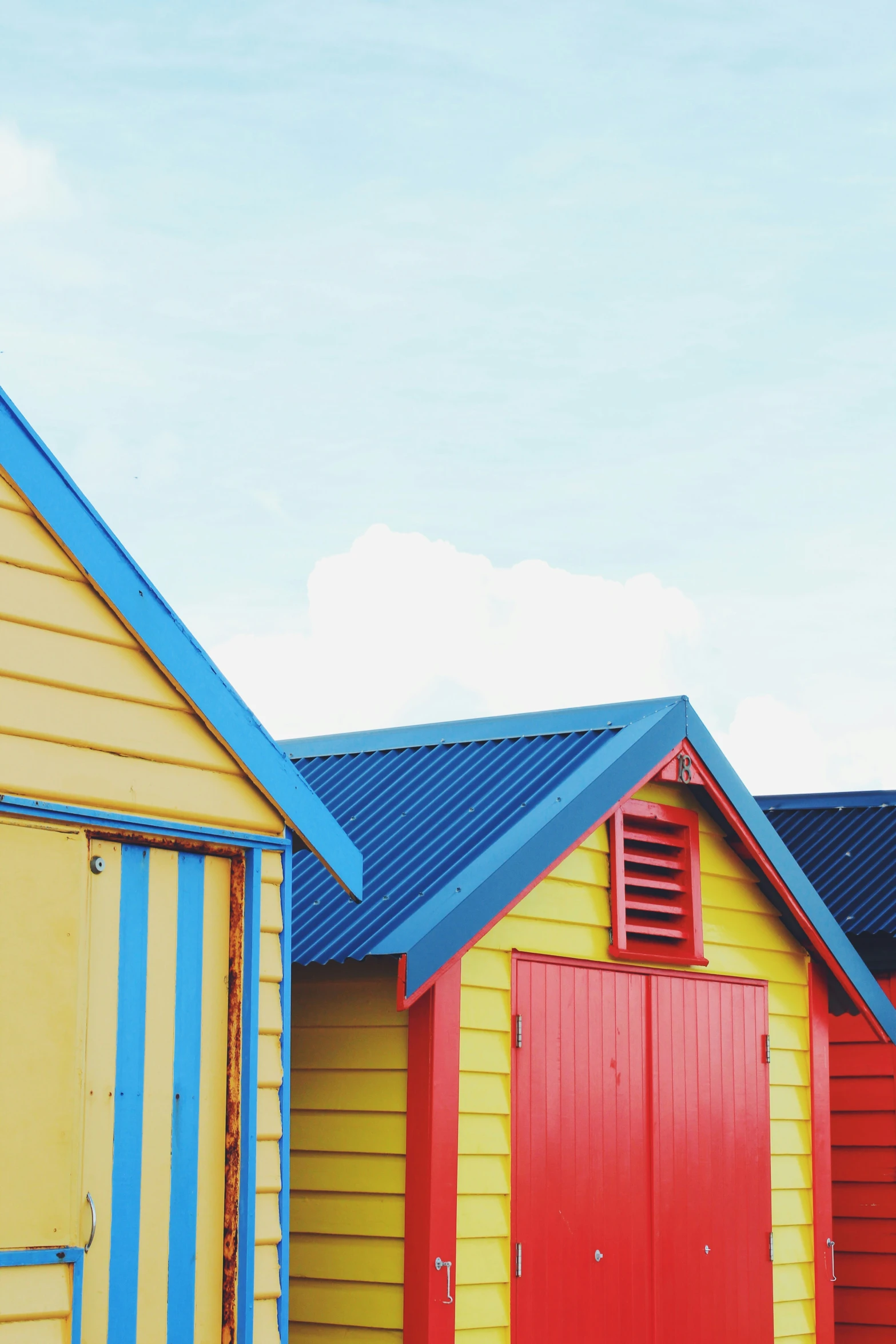 three beach huts sit side by side with a blue roof and a red one