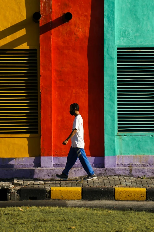 a man walking in front of a building that is painted yellow, red, and blue