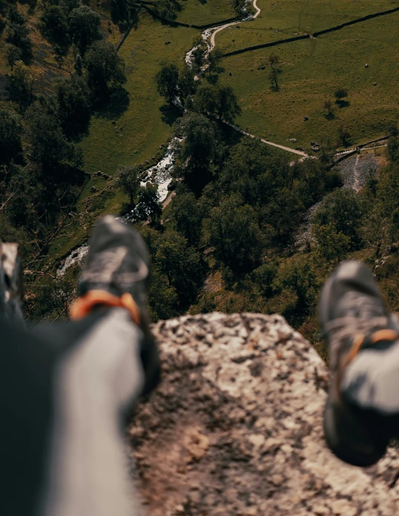 person in black shoes overlooking a stream and forest