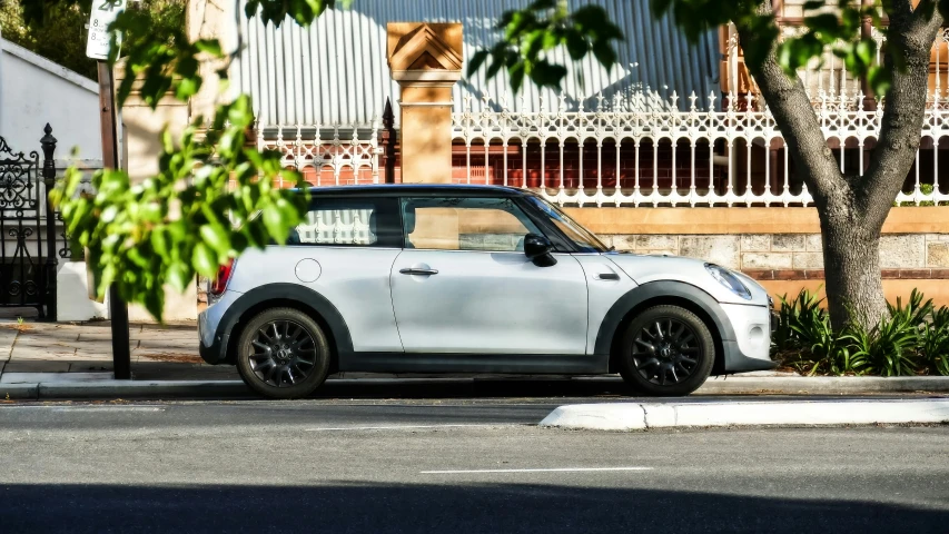 a small silver car parked at a curb next to a tree