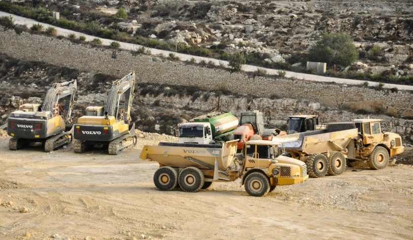 construction vehicles parked on a dirt area next to some hills