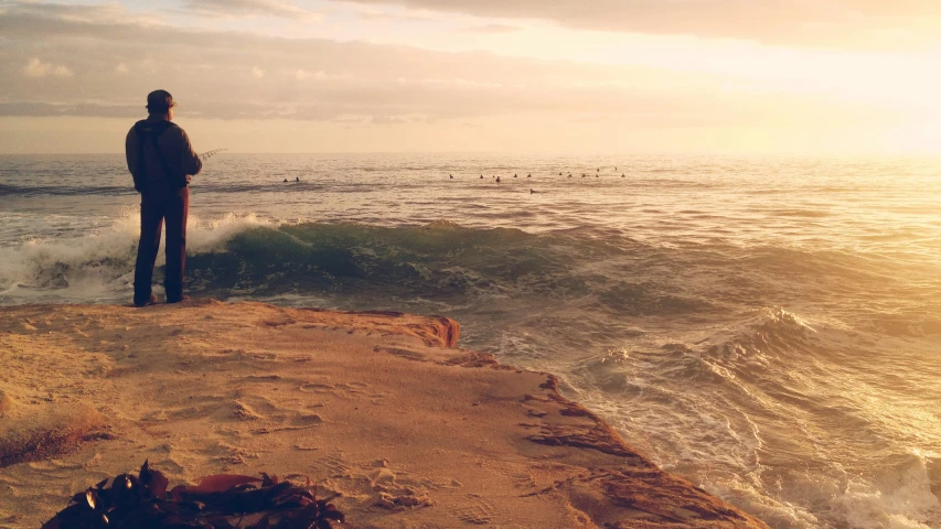 man watching surfboarders at sunset while standing on rocky shore