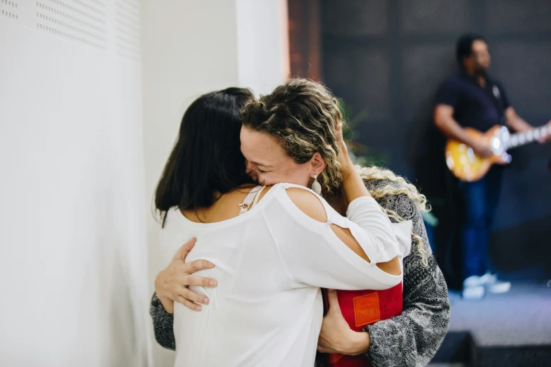 two women in the foreground hugging with other people in background