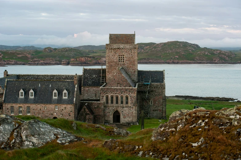 a stone building sits on top of a hill near a body of water