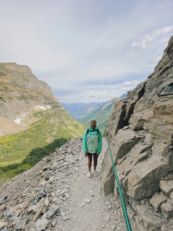 a woman in a green jacket is hiking on a rocky path